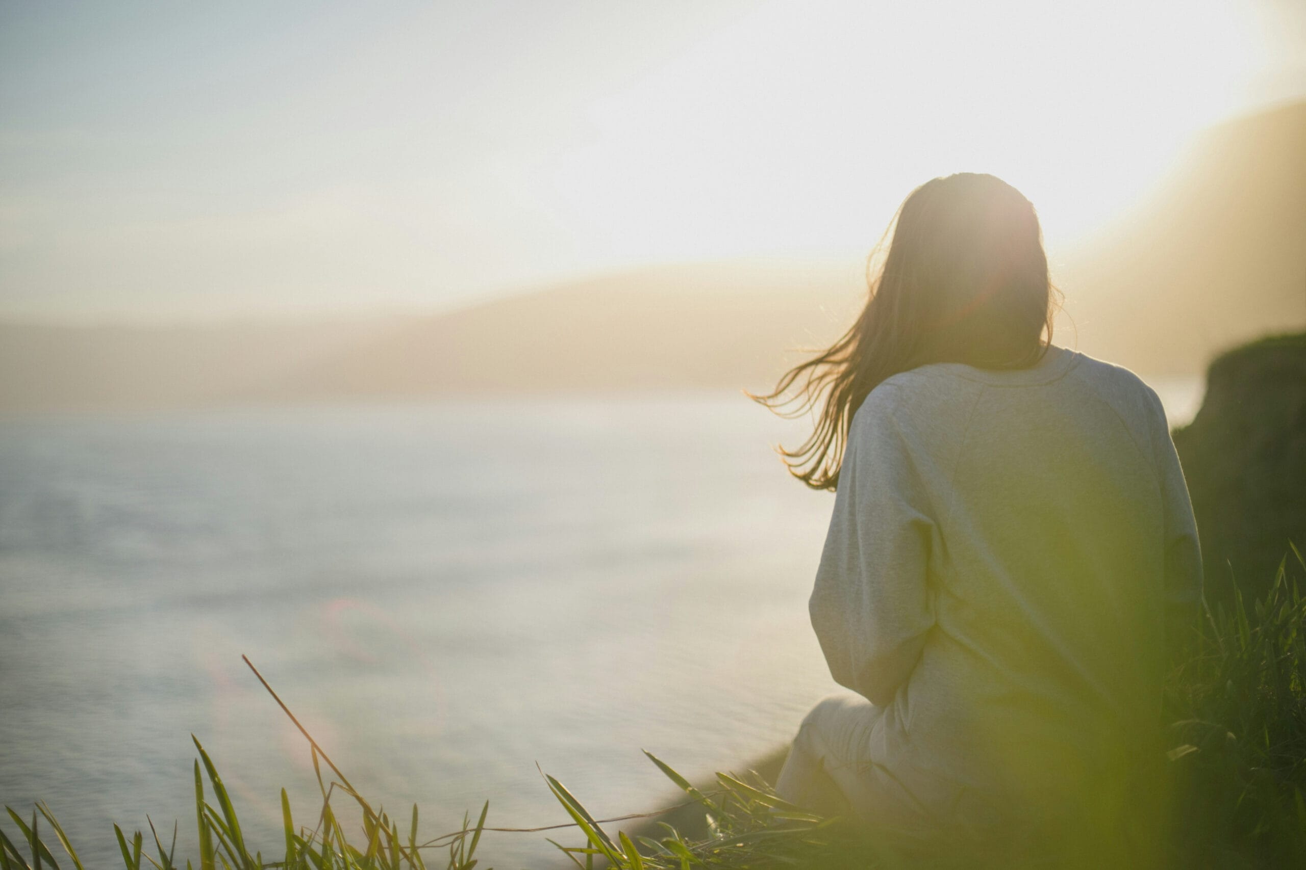 Person sitting facing a lake at sunset